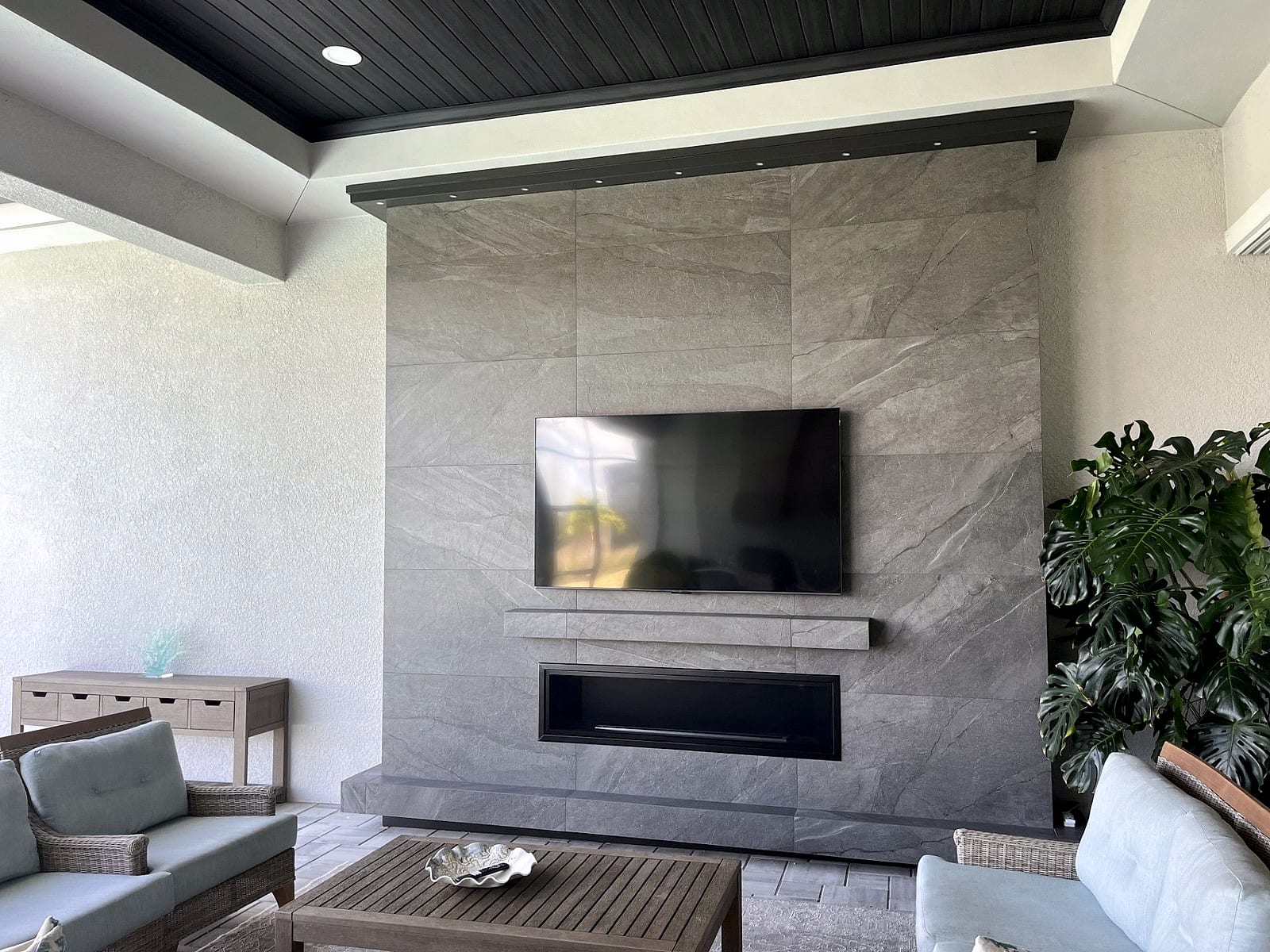 Tiled TV wall with linear fireplace beneath a dark plank ceiling